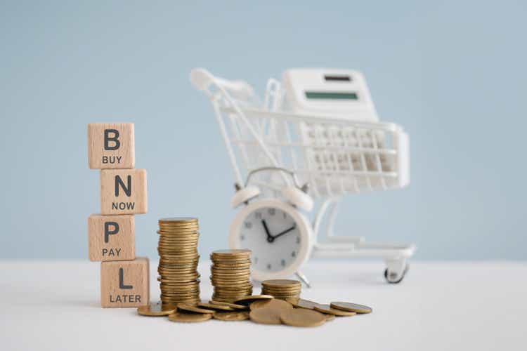 For buy now pay later , online shopping concept, wooden cube block with BNPL text and stack of coins, blurred white calculator in shopping cart and clock