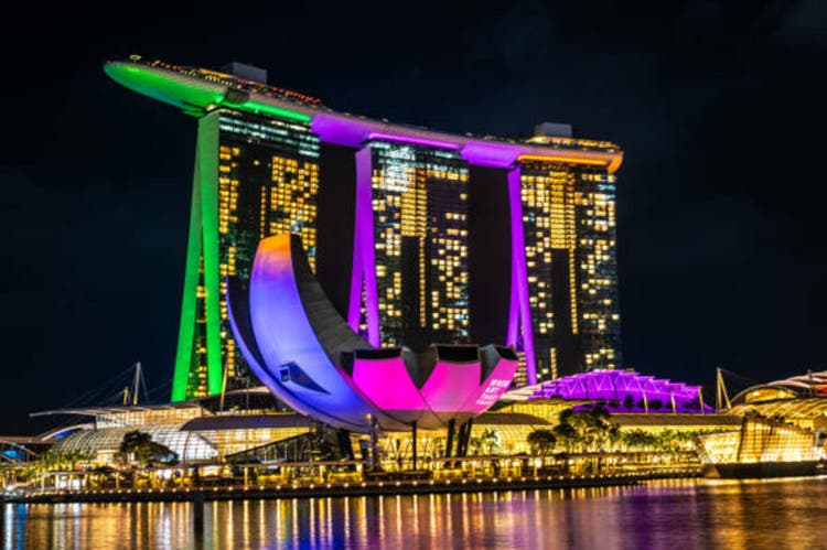 Marina Bay Sands hotel in Singapore of light at night, its bright illumination reflected in waters. ArtScience Museum and Helix Bridge join luminous cityscape