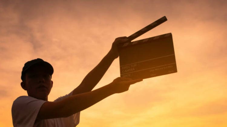 Teenage boy holding a film slate or film clapper board at sunset. new content creator, young filmmaker. movie industry concept.