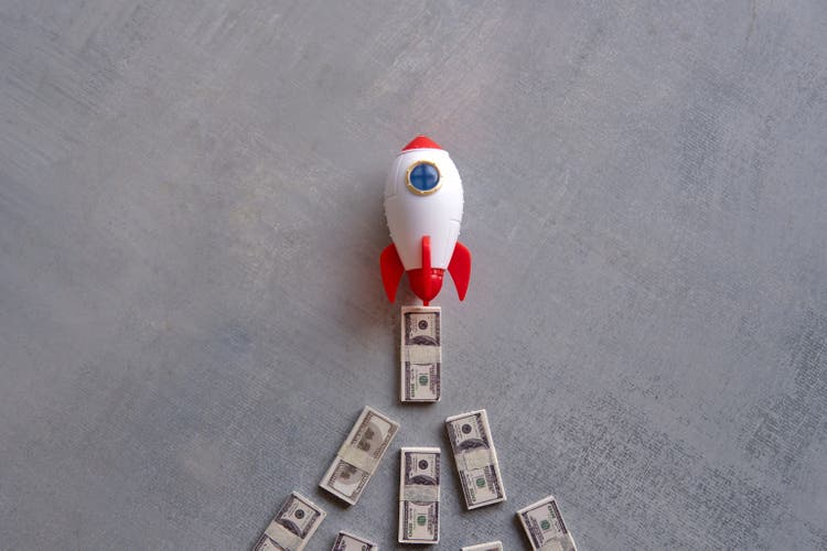 Rocket blasts off through a pile of money.
