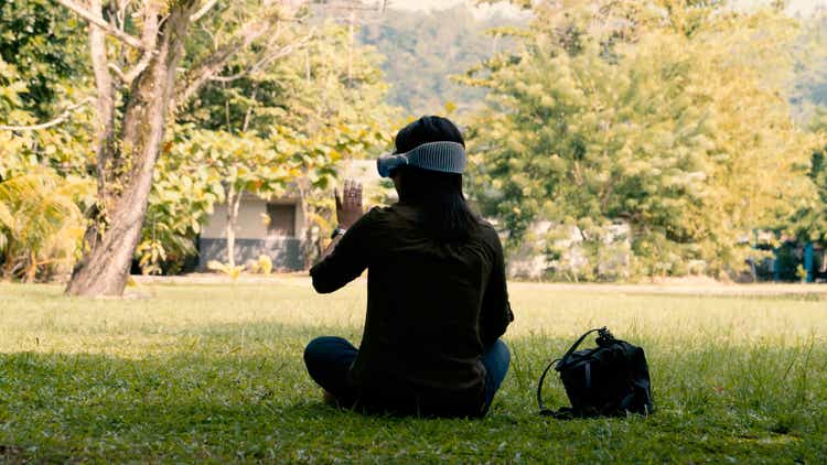 a woman sits in the park and wears apple vision pro glasses