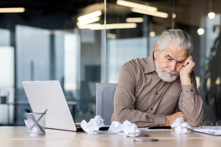 Upset frustrated gray haired boss sitting inside office at workplace, mature man old businessman in shirt working with laptop, unhappy with company achievement results and negative reports