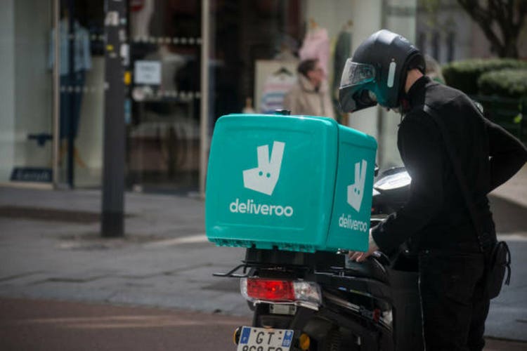 portrait of delivery man standing in the street near his deliveroo scooter