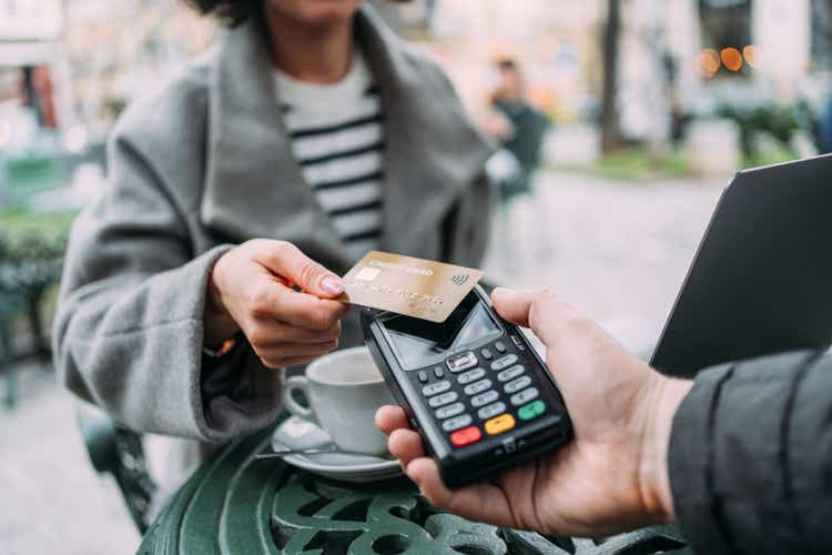 Young woman paying contactless with credit card in a sidewalk cafe.