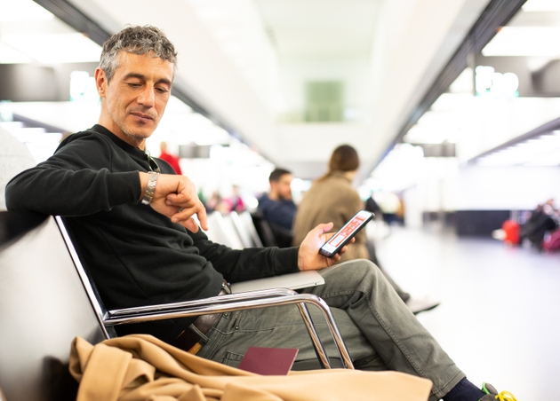 Man waiting at airport departure gate, checking the time
