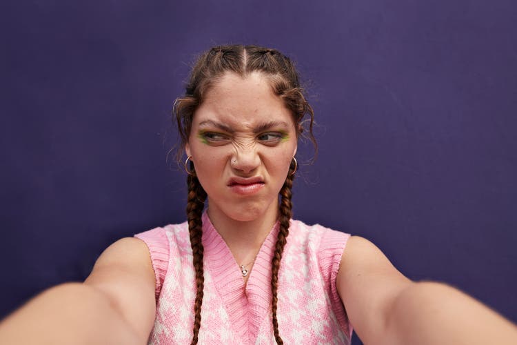 Young woman looking sideways grimacing while taking selfie