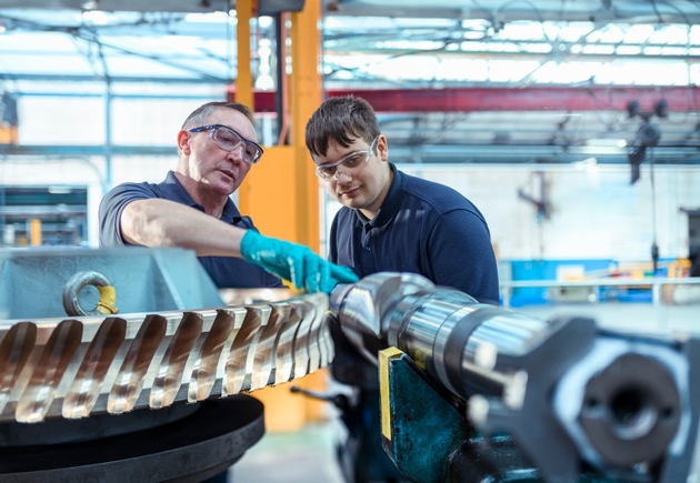 Engineer mentoring apprentice with worm gears in Engineering factory