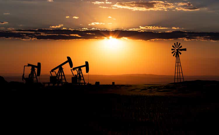 Oil pumps and wind mill during sunset.