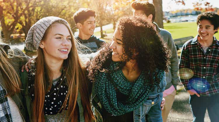 Teenager, walking and talking with friends in park, nature or social group outdoor together with funny conversation. Happy, teen and kids laugh at joke with best friend in community or relax in fall