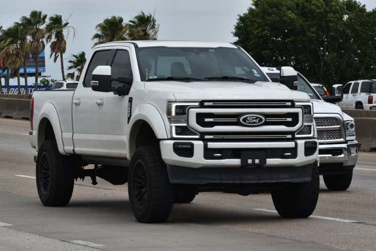 A portrait of a white Ford F-250 pick-up truck traveling down a highway in moderate traffic