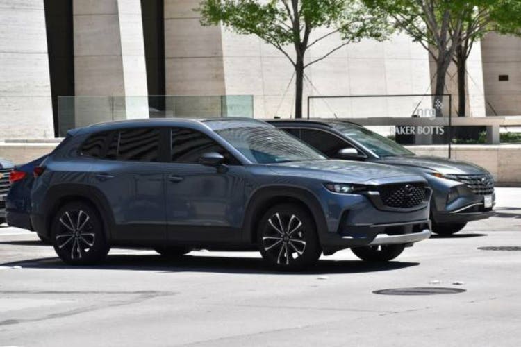 A portrait of a new Mazda CX-50 SUV traveling in a downtown district