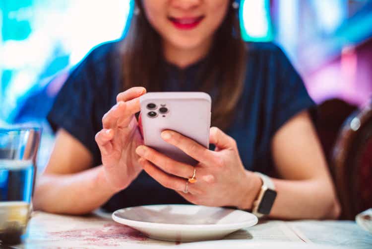 Young Asian woman using smart phone while enjoying meal in a local restaurant during vacation