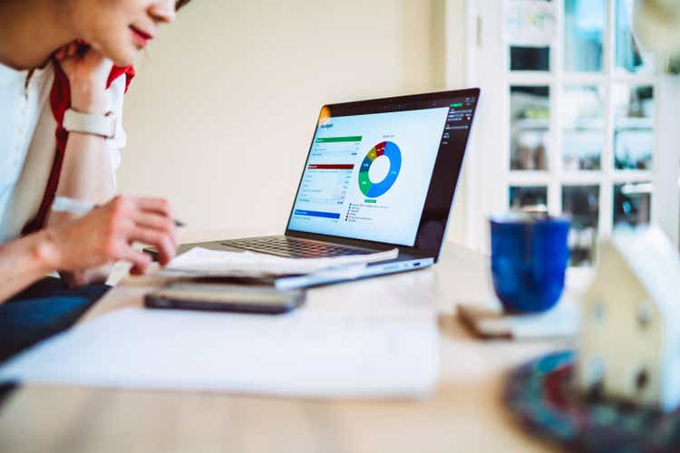 Young Asian woman managing home budget with the aid of AI financial app at home.