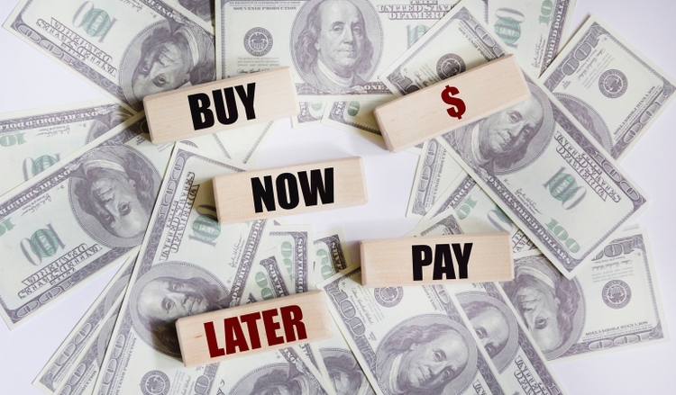 On a white table there are hundred dollar bills and wooden blocks with the inscription BUY NOW - PAY LATER