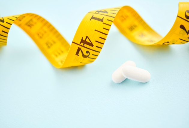 Tape measure with diet pills on a blue background