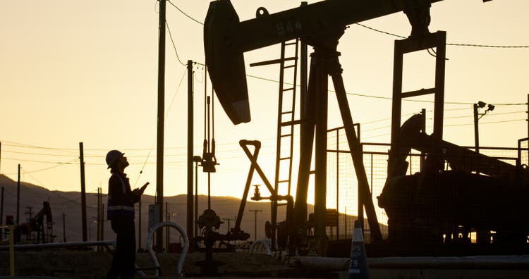 Oilfield Worker Looking up to Pump Jack with Sunset in Background