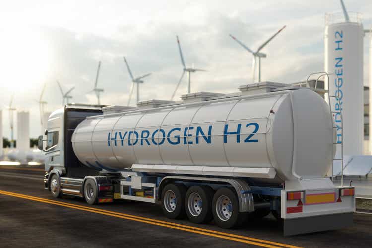 Rear View Of Hydrogen Transport Truck On The Road With Wind Turbines, Hydrogen Tanks And Solar Panels In Background