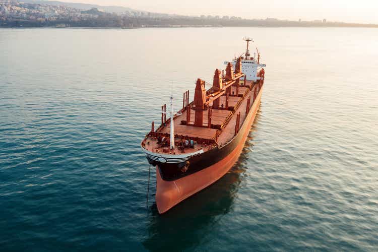 Aerial view sea vessel for transportation of cargo vessel at high speed is drifting near seaport of city at sunset. Ship on background of blue sea water. Import, export