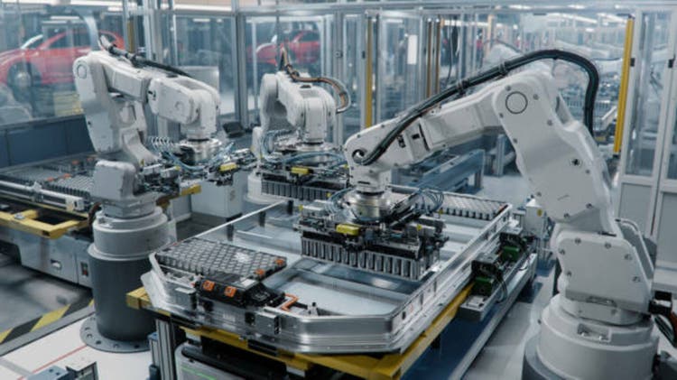 Row of White Robotic Arms at Automated Production Line at Bright Modern Factory. Industrial Robot Arms Assemble Lithium-Ion EV Battery Pack. Electric Car Manufacturing Inside Automotive Smart Factory