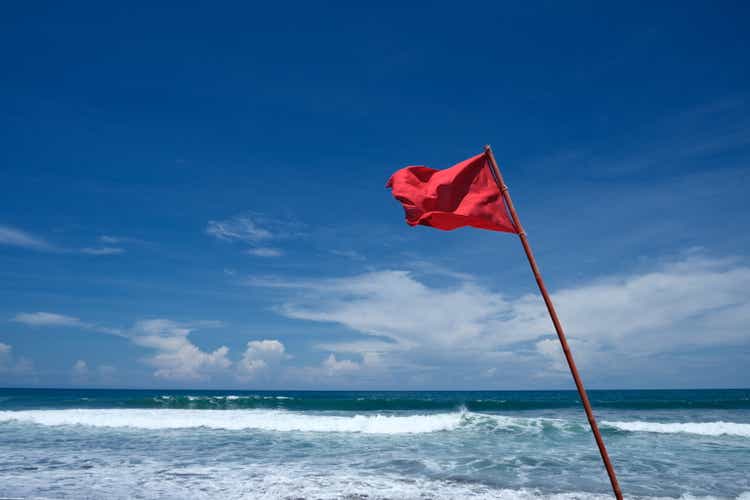 Red warning flag waving on a sunny beach, signaling hazardous conditions