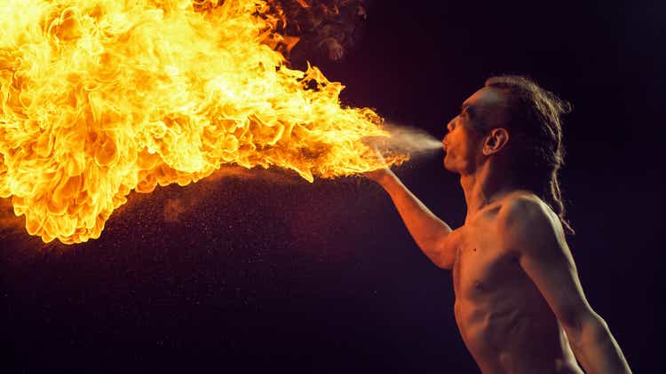 Male Fire Performer With Dreadlocks Skillfully Exhales Massive Fireball, Creating Spectacular Display of Flames and Sparks Against Dark Background, Cinematic Intensity and Artistry of Fire Breathing.