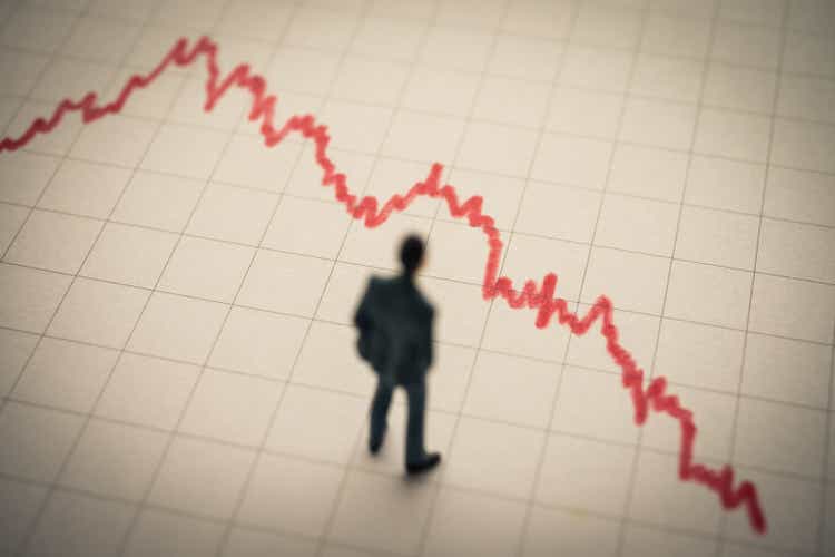 Businessman looking at falling down red graph tensely.