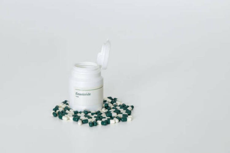 A pill bottle of 1mg finasteride capsules with several capsules scattered around