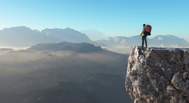 Hiker on top of a mountain with large misty landscape in front of him
