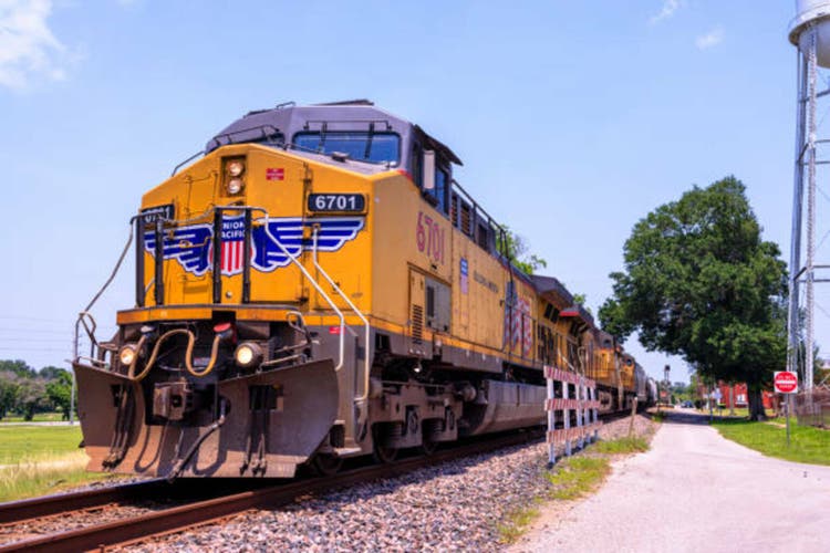 Freight transport powers through rural America. Yellow Union Pacific locomotive 6701 leads cargo train on single track