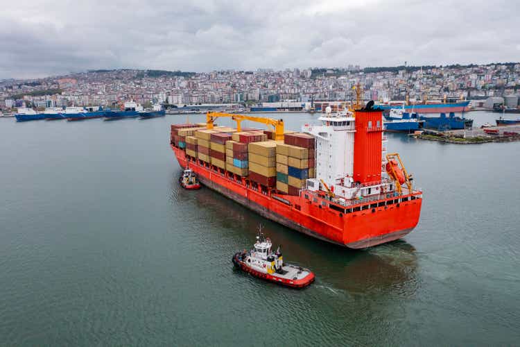 Aerial view of Cargo container ship carrying container and running with tugboat for import goods to cargo container terminal for customs. Concept of logistics transportation and shipping.