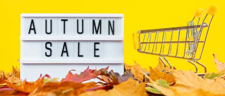 Autumn sale and discount concept. Shopping cart and fallen colored leaves on yellow background. Creative composition for advertising.