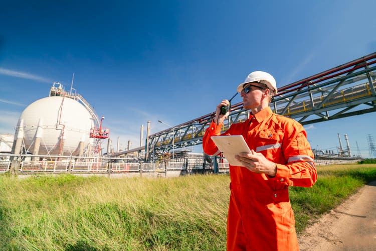 A safety engineer in an orange jumpsuit and white hard hat uses a radio to communicate at site, ensuring smooth operations. The image highlights the importance of safety, communication, and coordination in industrial settings.