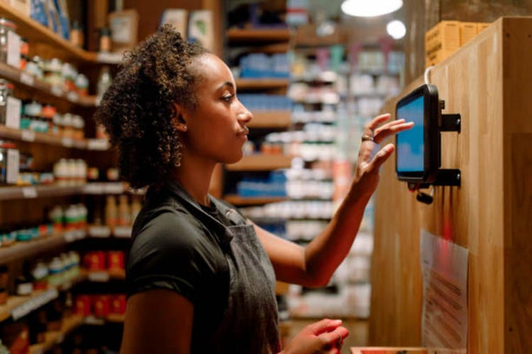 Side view of female owner using digital tablet mounted on wooden wall while working at supermarket