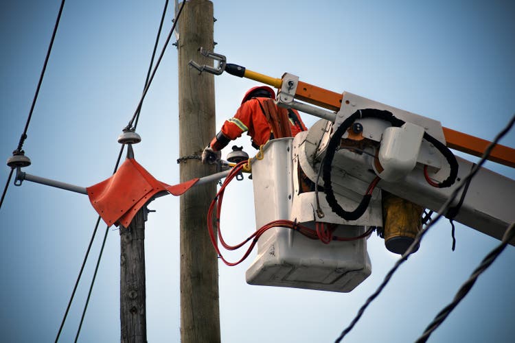 Trabajador de líneas eléctricas reparando líneas eléctricas usando una plataforma aérea