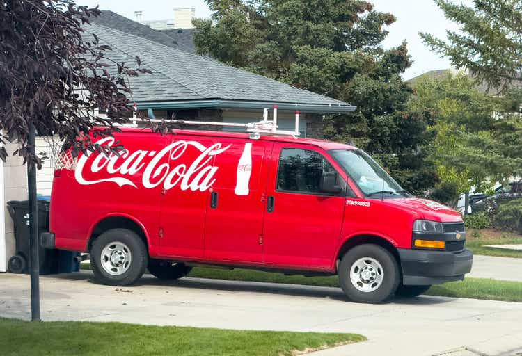 A van branded with the Coca-Cola logo and a bottle graphic. A red Chevrolet Express van parked in a residential driveway.