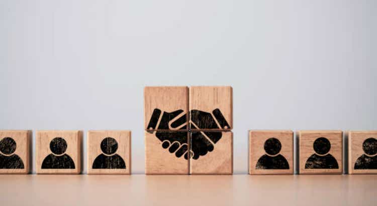A manual printing screen on a wooden block cube between the human icon of the commercial deal and the concept of agreement.