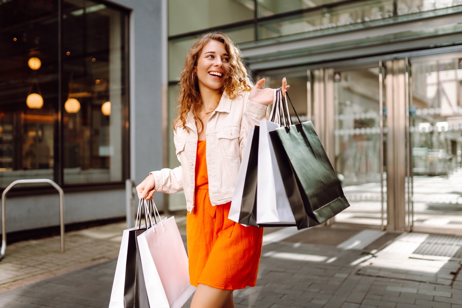 Cheerful woman enjoying shopping on a sunny day while carrying multiple bags in an urban setting.