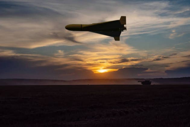 A military drone flies over a peaceful field, the evening illumination