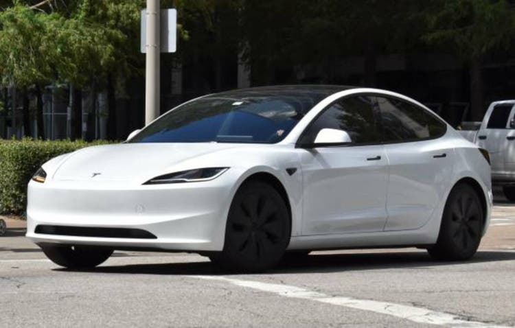 A portrait of a white Tesla Model 3 EV cruising in a downtown district