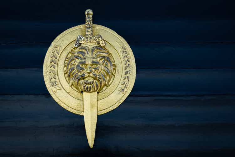 Shield with lion head isolated on dark background. Shield and sword in gold color