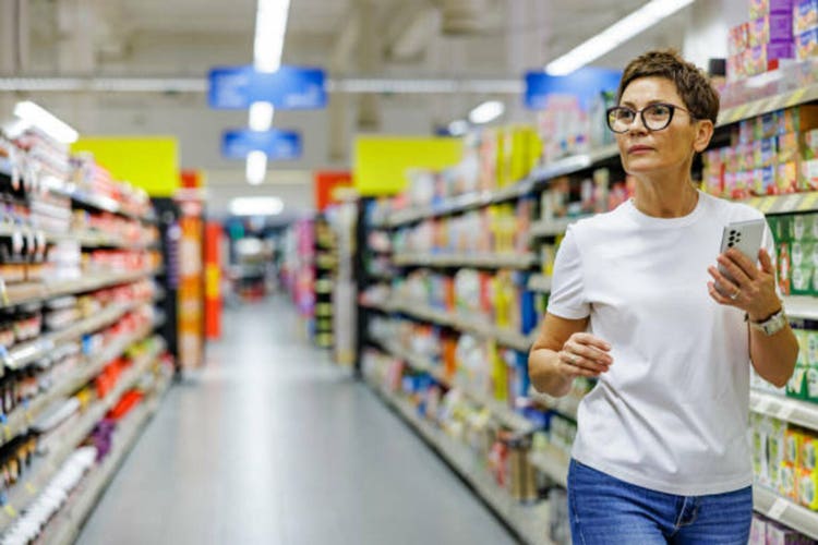 Beautiful lady searching grocery in supermarket following shopping list on smartphone