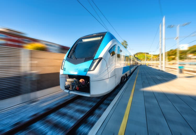 High-speed blue passenger train moving at railway station platform at sunset. Train station. Modern railway transportation concept with blurred motion effect. Railroad. Commercial transport. Slovenia