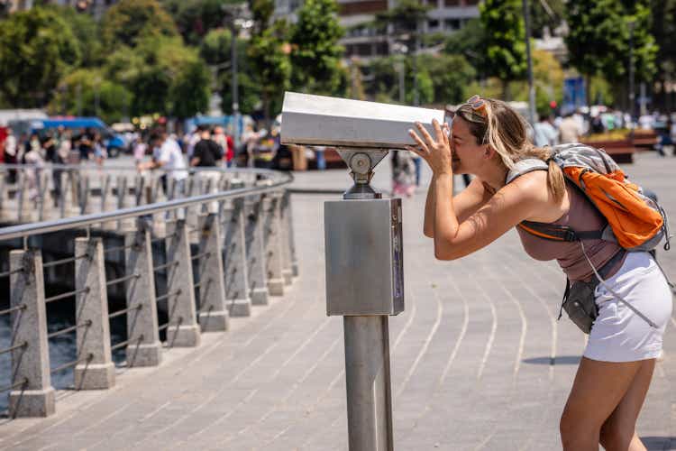 Woman peering through coin-operated telescope, exploring.