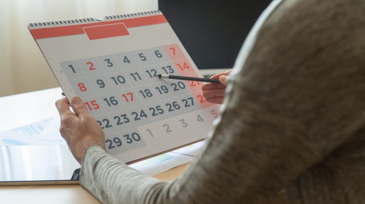 Person Organizing Daily, Weekly, and Monthly Activities Using a Calendar. Planning and Scheduling Work, Personal Tasks, Family, Vacations, School, and Appointments in Advance for Productivity.