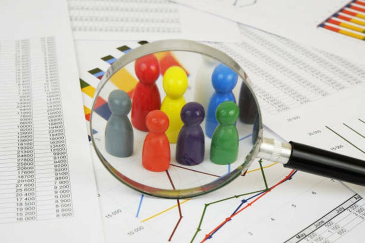Different colored wooden people figures under magnifying glass on financial report.