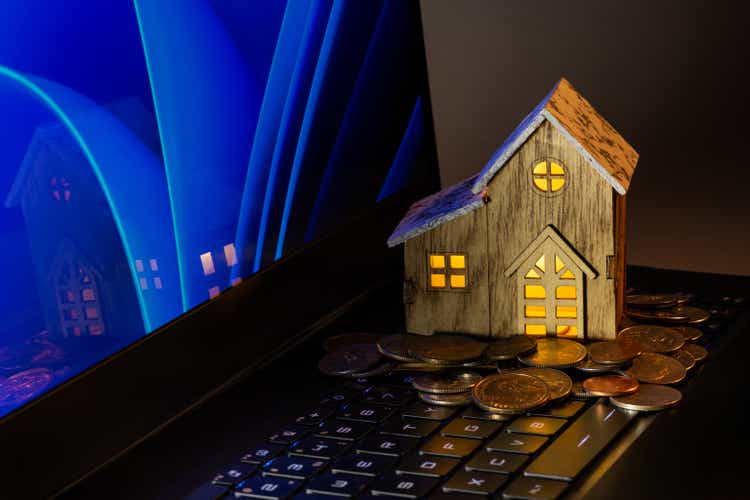 Symbolic wooden house and US coins on laptop keyboard