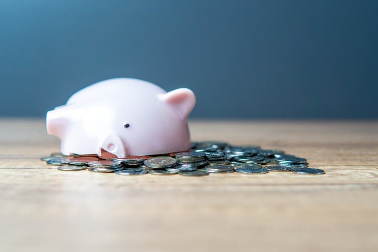 A broken pink piggy bank spilling over with a pile of coins on a wooden table.