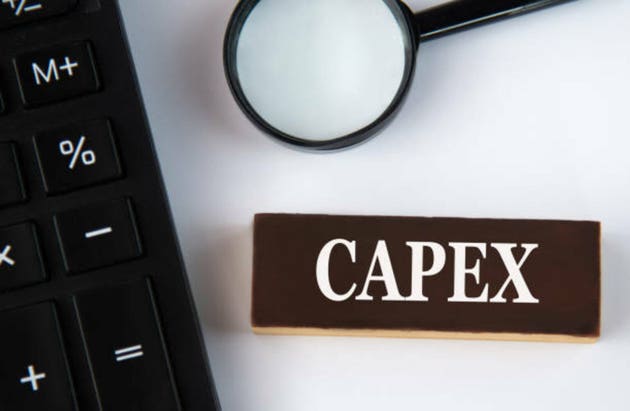 CAPEX - word on a brown wooden block with a calculator and magnifying glass in the background