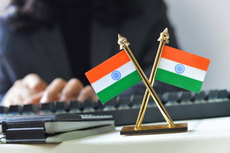 Horizontal photograph of two crossing Indian National flags making a cross on the desk of one unrecognisable out of focus or defocused person government official who is working typing on a keyboard page on her desk