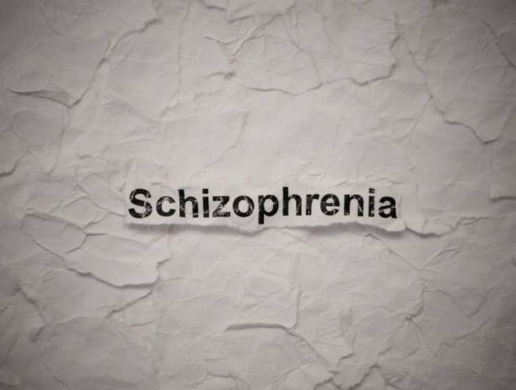 Crumpled piece of paper with word Schizophrenia on torn white paper pieces background.